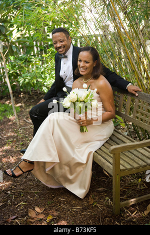 Happy African-American bride and groom sitting on bench Stock Photo