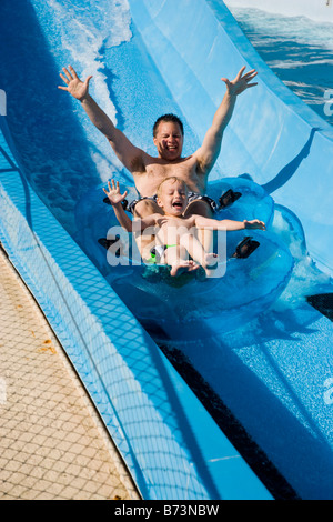 Father and son sliding down water slide together on innertube in water park Stock Photo