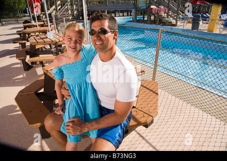 Daughter sitting on father's lap at water park at table Stock Photo