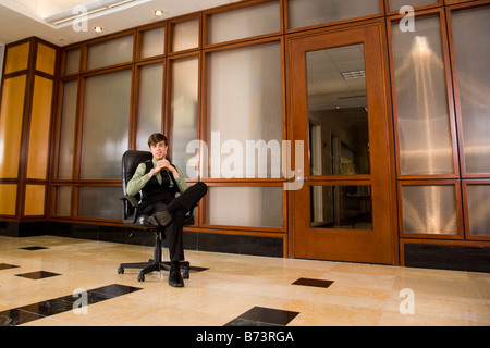 Young businessman sitting on office chair alone in lobby Stock Photo