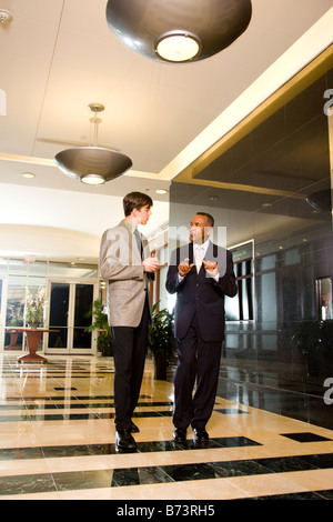 Businessmen walking through lobby of office building while talking Stock Photo