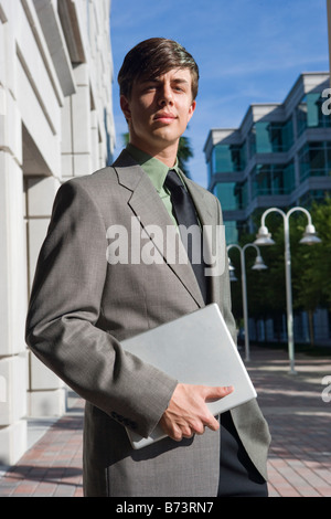 Young businessman standing outside office building holding laptop Stock Photo