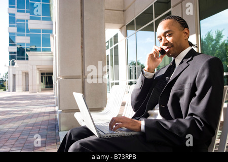 African-American businessman outside office building using laptop and mobile phone Stock Photo
