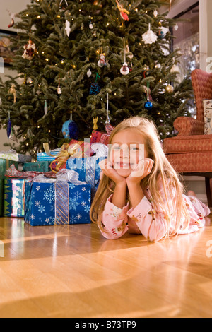 Young girl lying on floor next to Christmas tree and presents Stock Photo