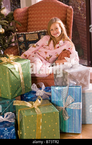 Young girl sitting in chair next to Christmas tree and presents Stock Photo