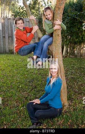 Children climbing tree with mother in backyard Stock Photo