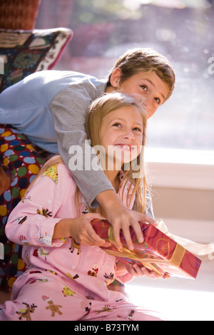 Portrait of bother and sister shaking Christmas gift on living room floor Stock Photo