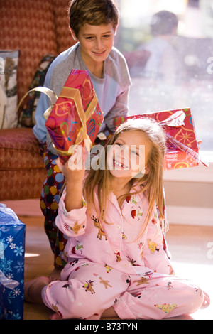Portrait of bother and sister shaking Christmas gift on living room floor Stock Photo