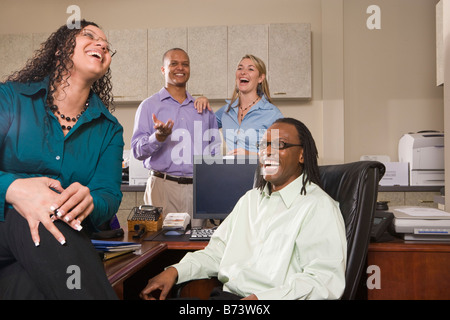 Four multi-racial businesspeople laughing in office around desk Stock Photo