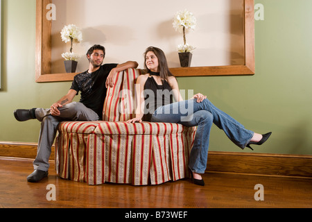 Young man and woman sitting together on ottoman indoors Stock Photo