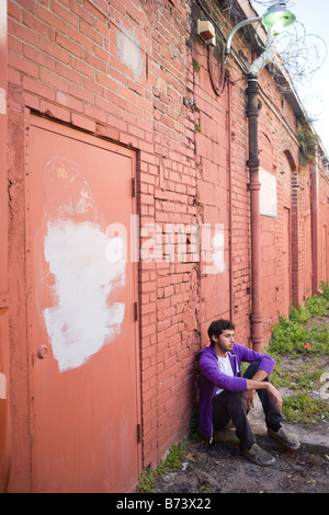 Young man hanging out in alleyway leaning again brick wall Stock Photo