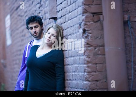 Young couple leaning up against brick wall of building outside Stock Photo