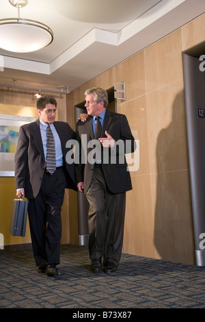 Two multi-racial businessmen discussing in front of elevators in office Stock Photo