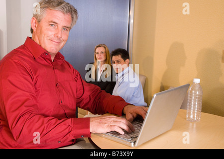 Middle-aged male office worker using laptop, co-workers in background Stock Photo