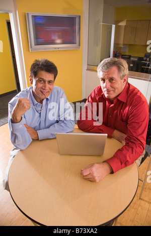 Two multi-racial middle-aged businessmen using laptop in office Stock Photo