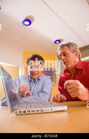 Two multi-racial businessmen discussing laptop in office Stock Photo