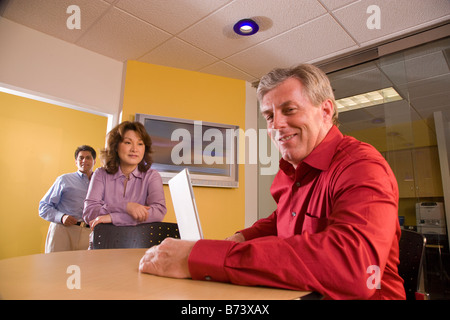 Three multi-racial businesspeople in office, man using laptop in foreground Stock Photo