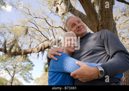 Low angle view of senior couple hugging below tree, smiling Stock Photo