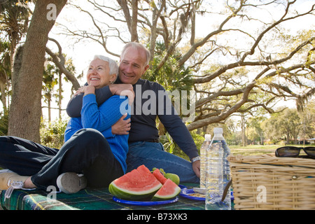 Senior couple sitting on picnic table in garden with fruits, looking away Stock Photo