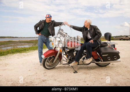 Happy senior biker couple with motorcycle holding hands on dirt road Stock Photo