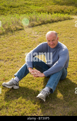 Senior man sitting on grass in park Stock Photo
