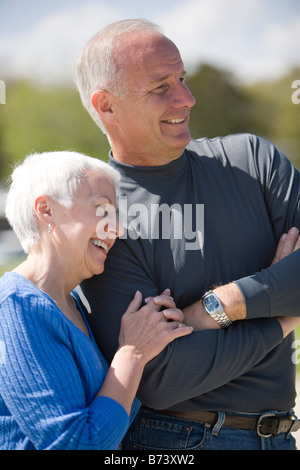 Side view of senior couple standing with arm in arm outdoors on sunny day Stock Photo