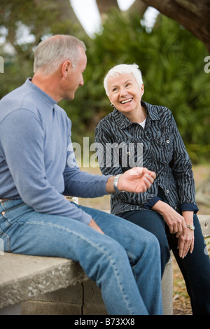 Happy senior couple sitting outdoors on park bench, smiling Stock Photo