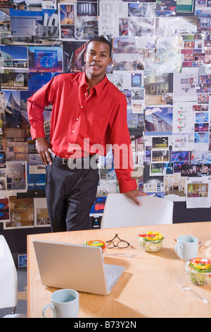 Young man standing in office with cup and bowl on desk Stock Photo