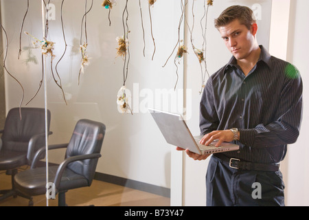 Young man using laptop, standing outside empty conference room Stock Photo