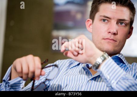 Closeup of young businessman sitting in office holding eyeglasses Stock Photo