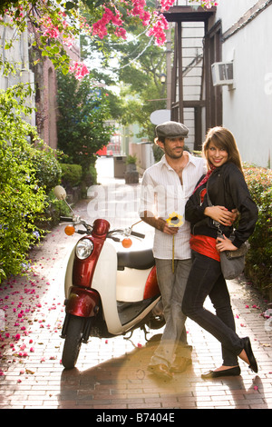 Young couple standing by motor scooter in alleyway Stock Photo