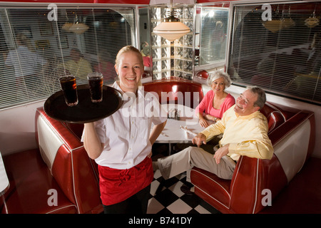 Waitress serving drinks to senior couple seated in old-fashioned diner