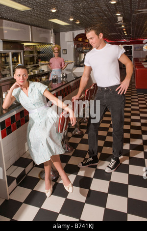 Young woman sitting at counter in diner ignoring boyfriend, 1950s style Stock Photo