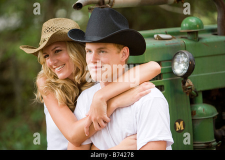 Young couple wearing cowboy hats sitting on tractor outdoors Stock Photo