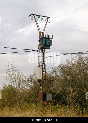 High voltage electric pillar in forest against clouds, with low current unit Stock Photo