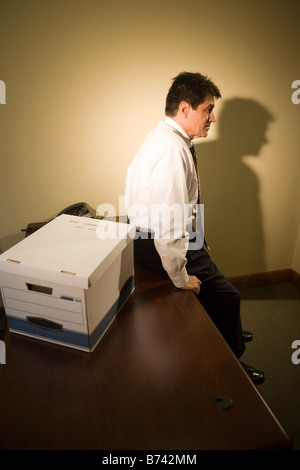 Mature Hispanic businessman leaning on desk in empty office with box Stock Photo