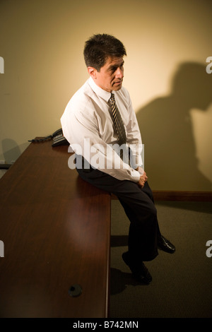 Mature Hispanic businessman leaning on desk in empty office Stock Photo