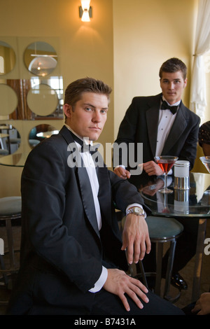 Two young adult men wearing tuxedos having drinks in restaurant lounge Stock Photo