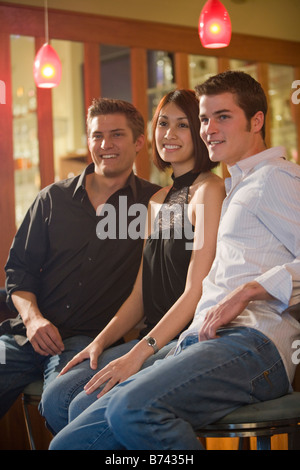 Three young adult friends smiling together at restaurant bar Stock Photo