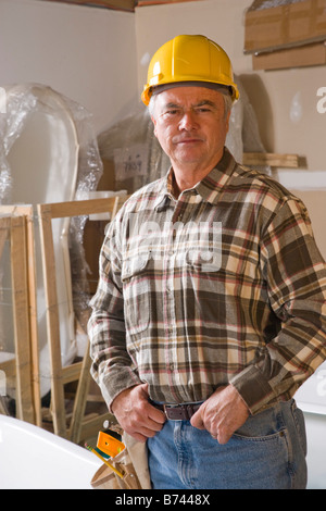 Senior man in hard hat standing indoors at construction site Stock Photo