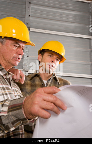 Male construction workers wearing hard hats looking at plans Stock Photo