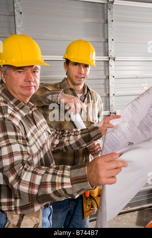 Male construction workers wearing hard hats looking at plans Stock Photo