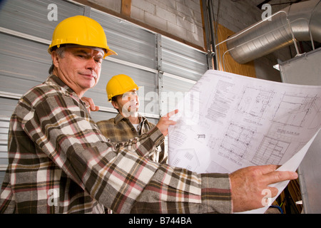 Male construction workers wearing hard hats looking at plans Stock Photo