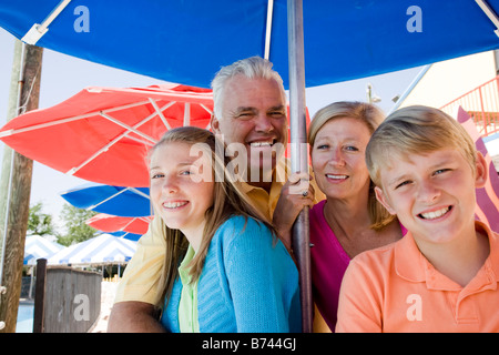 Portrait of family sitting together under shady umbrella Stock Photo