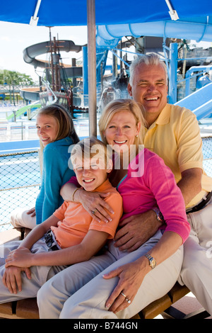 Portrait of family sitting together under shady umbrella at water park Stock Photo