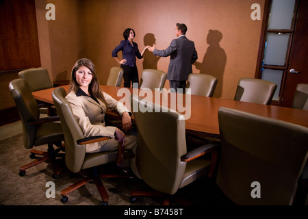Woman sitting in chair, businesspeople in background Stock Photo