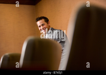 View of businessman standing and smiling, chairs in foreground Stock Photo