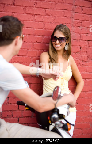 Young man on motor scooter talking to woman leaning against red brick wall Stock Photo
