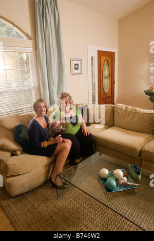 Two women sitting with wine glasses on sofa in living room Stock Photo