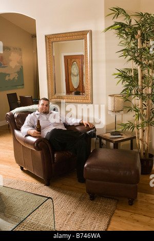 Man sitting with beer bottle on arm chair in living room Stock Photo